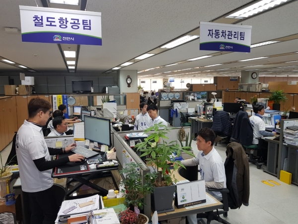 18명의 천안시 교통정책과 직원들이 매주 월요일마다 중부권 동서횡단철도 건설사업의 신속한 추진을 건의하는 내용이 새겨진 단체복을 입고 근무