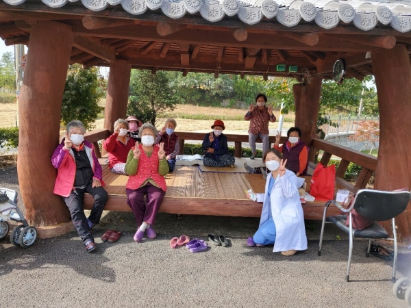 프로그램에 참여한 진료소장과 지역주민이 마을 정자에서 기념사진을 찍고 있다