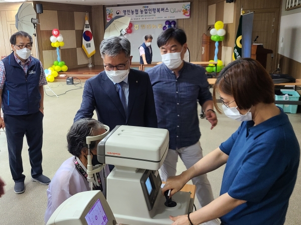 길정섭 충남세종농협 본부장(가운데)이 2021년 첫 번째로 진행된 농업인 행복버스 봉사활동에서 무료 검안을 받고 있는 농업인을 격려하고 있다.