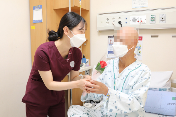 병동 간호사가 어르신 환자에게 카네이션을 드리고 있다.